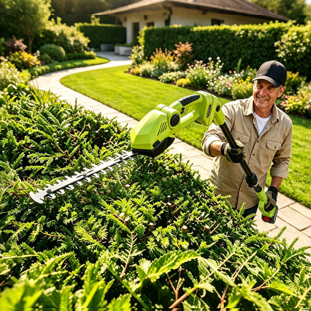 A man wearing a black cap and work clothes uses a bright green cordless hedge trimmer to cut dense green bushes in a sunny, well-landscaped garden.